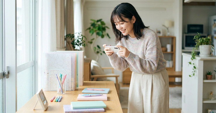 デスクに並べたクリアファイルをスマホで撮影する女性